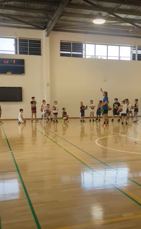 Coach James leading a group basketball session with kids in a gym